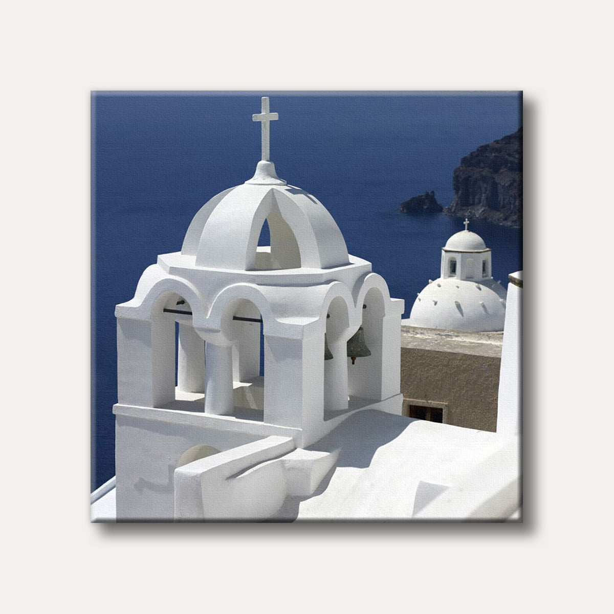 A close-up of a classic white church with a bell tower and dome, overlooking the deep blue sea and distant land, characteristic of Greek islands.