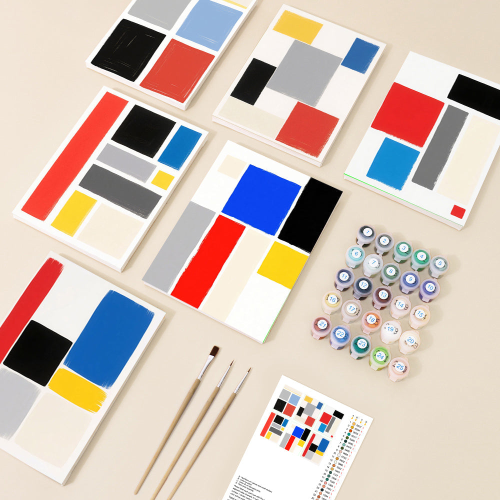 An overhead view of several incomplete abstract geometric paintings in the style of Mondrian, alongside paint pots, brushes, and a colour guide, showcasing a DIY paint by number kit.
