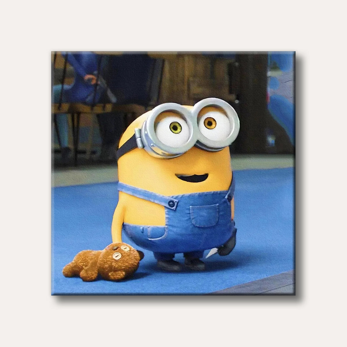 A yellow Minion character wearing blue overalls and large goggles stands beside a brown teddy bear on a blue floor, depicted in a cheerful cartoon style.