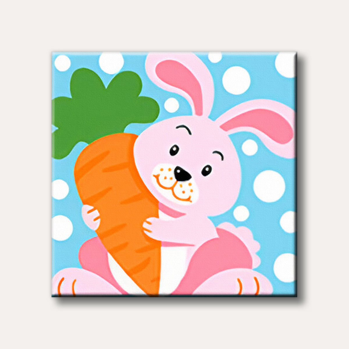 A cartoon-style pink bunny rabbit with long ears holding a large orange carrot, set against a light blue background with white polka dots, designed for a paint by numbers kit.