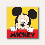A cheerful illustration of Mickey Mouse with his iconic smile peeking over a red banner displaying his name, against a vibrant yellow background, in a classic cartoon style.